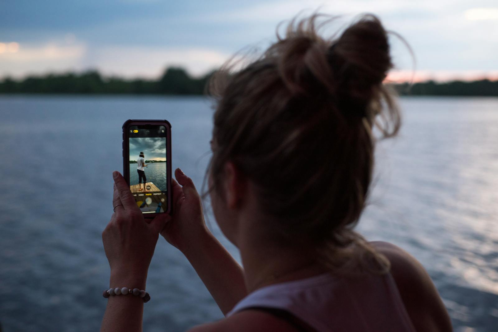 A woman captures a scenic view of Beaver Lake, Canada at sunset, using her smartphone.